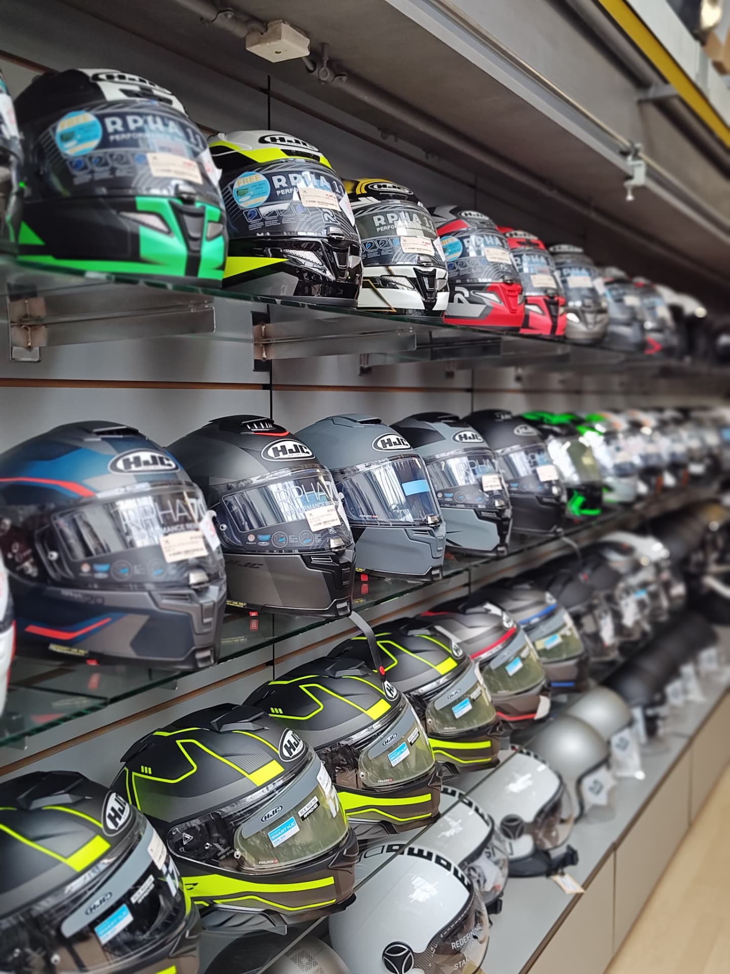 Nahaufnahme von HJC-Helmen auf Glasregalen im Helm-Bereich des Moto-Center WEST Nahaufnahme von HJC-Helmen auf Glasregalen im Helm-Bereich des Moto-Center WEST